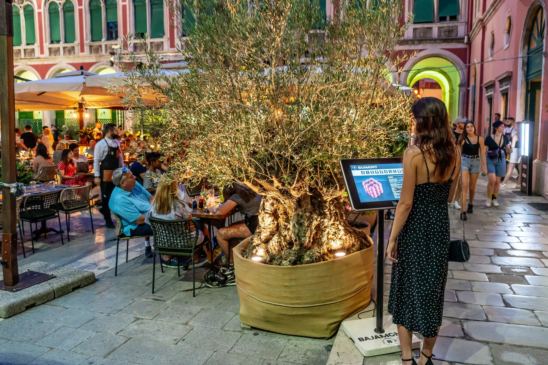 Gošća čita meni na NIKA24 uređaju ispred restorana Bajamonti na Trgu Republike u Splitu